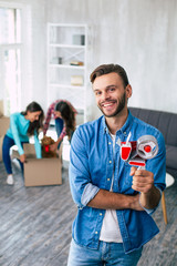 Wall Mural - Some work to do. Handsome man is holding a scotch tape in his left hand while his wife and daughter are packing their belongings and preparing to move into the new house.