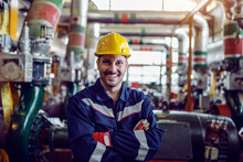 Smiling Caucasian Energy Plant Worker Dressed In Working Clothes And With Helmet On Head Standing With Arms Crossed.