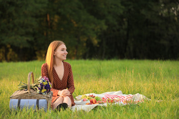 Canvas Print - Beautiful young woman with picnic basket sitting on blanket in park