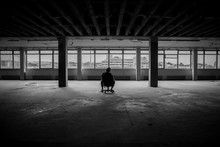 Man Sitting In Front Of A Large Window In An Empty Hall Of An Abandoned Building - Black And White