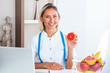 © Graphicroyalty - Portrait of young smiling female nutritionist in the consultation room. Nutritionist desk with healthy fruit, juice and measuring tape. Dietitian working on diet plan.