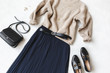 Blue midi pleated skirt, beige knitted sweater, small black cross body bag, belt, loafers (flat shoes) on grey background. Overhead view of women's casual day outfit. Flat lay, top view. Women clothes