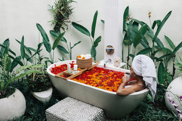 Wall Mural - Woman relaxing in outdoor bath with flowers in Bali spa hotel.