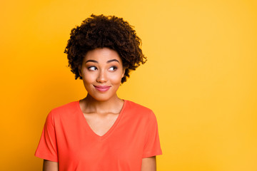 Photo of amazing dark skin lady looking side empty space with cunning smile wear orange v neck t-shirt isolated yellow color background