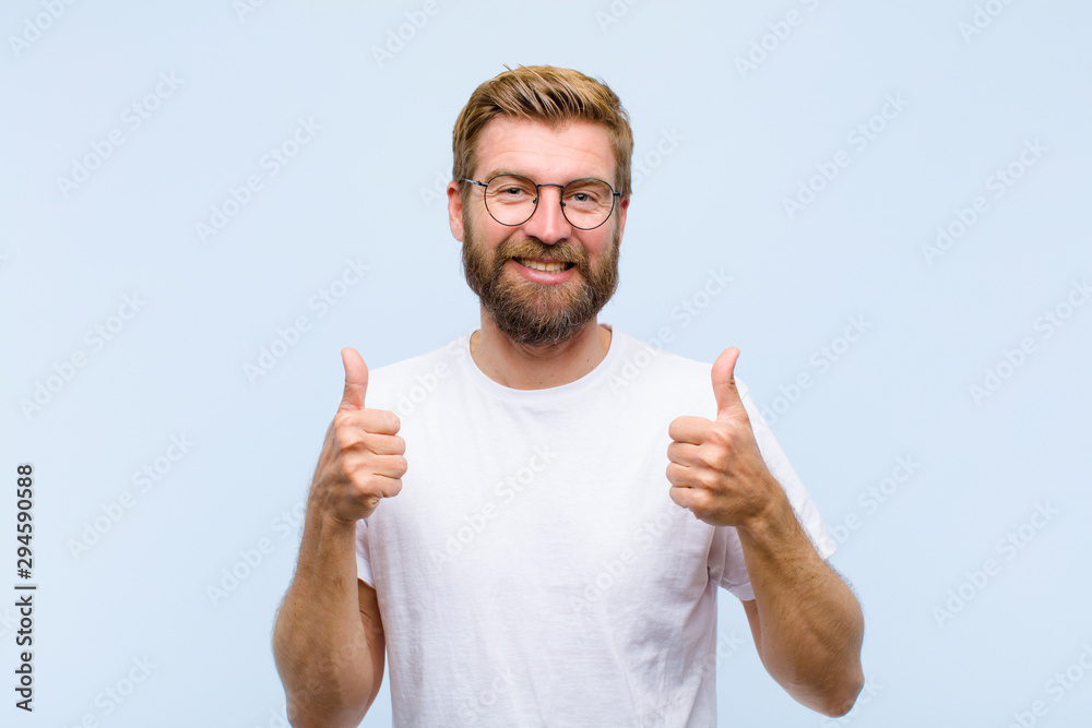 young blonde adult man smiling broadly looking happy, positive, confident and successful, with both thumbs up - obrazy, fototapety, plakaty 