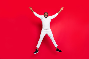 Wall Mural - Full size photo of excited dark skin handsome guy jumping high rejoicing having best x-mas party time wear white sweater trousers isolated red background