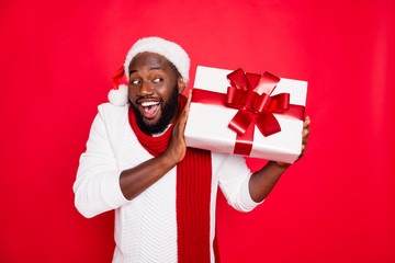 Portrait of amazed funky dark skin man wear santa claus headwear hold big package receive on x-mas time celebration scream wow feel interested wear style pullover isolated over red color background