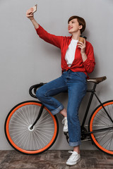 Sticker - Full length image of woman taking selfie photo on smartphone by bicycle