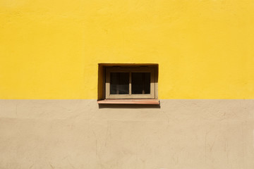 Colorful wall fragment with small window in the middle background. Yellow and beige house wall on sunny summer day close up.