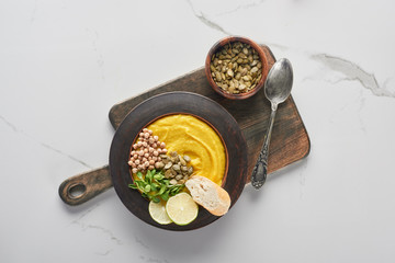 Sticker - top view of autumnal mashed pumpkin soup on wooden cutting board with seeds and spoon on marble surface