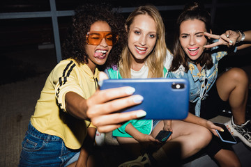 Wall Mural - Girls friends at night on street take a selfie mobile phone.