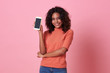 Portrait of happy young african woman showing at blank screen mobile phone isolated over pink background.