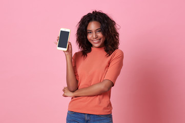 portrait of happy young african woman showing at blank screen mobile phone isolated over pink backgr