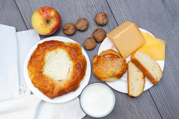 Fresh homemade buns with sesame and cheese on wooden background with glass of milk, apple, nuts.