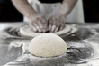 Ball of pizza dough on table with chef hands knead the dough in background.
