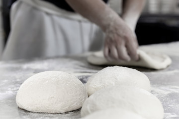 Wall Mural - Ball of pizza dough on table with chef hands knead the dough in background.