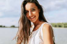 Close-up Outdoor Portrait Of Beautiful Happy Young Woman Smiling Broadly With Toothy Smile With A Windy Blowing Long Hair In The Park, Posing On Nature Background.
