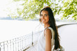© iuricazac - Rear view shot of happy young brunette woman smiling broadly with a windy blowing long hair walking in the park next to the lake.