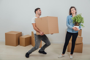 Man can not hold heavy carton boxes anymore, but he doesn't know where to put them. His wife is standing with flowerpot in hands, dreaming.