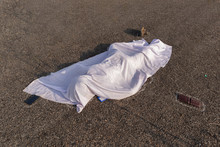 Concept Of Road Accident Scene, High Angle View Of Chalk Outlined Dead Body Covered Under White Cloth Laying On Road.