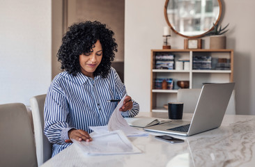 Smiling female entrepreneur going through paperwork at her dining table