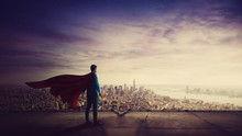 Rear View Confident Businessman, Red Cape Suit, As Hero Stands On The Rooftop Of A Skyscraper Looking Over The City Horizon. Superhero Leadership And Success Concept. Surreal Super Power Metaphor.
