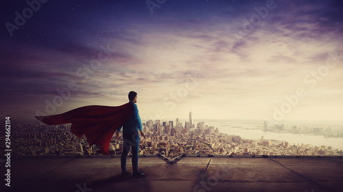Cuadros en Lienzo Rear view confident businessman, red cape suit, as hero stands on the rooftop of a skyscraper looking over the city horizon