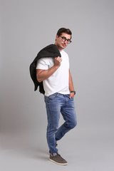 Wall Mural - Handsome young man in casual clothes with black jacket and glasses on grey background