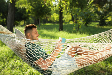 Poster - Young man reading book in comfortable hammock at green garden