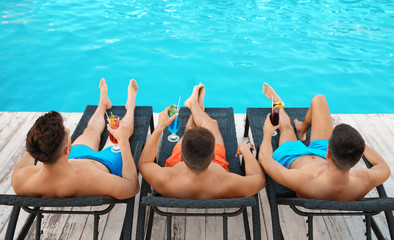 Sticker - Happy young friends with refreshing cocktails relaxing on deck chairs near swimming pool