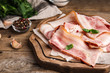 Board with slices of raw bacon on wooden table, closeup