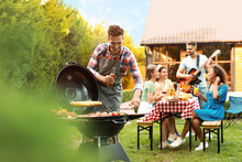 Group Of Friends At Barbecue Party Outdoors. Young Man Near Grill
