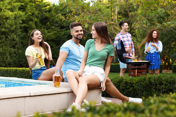 Canvas Print - Happy friends with drinks at barbecue party near swimming pool outdoors