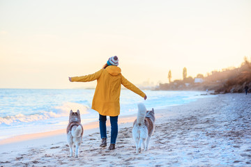 red-haired girl in a yellow rain coat and two husky dogs on the beach