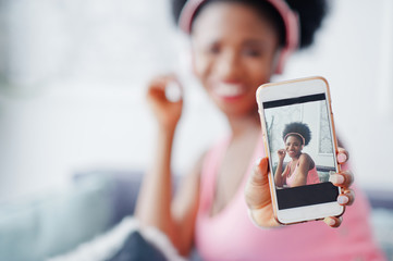 Photo of screen mobile phone young african american woman sitting on the couch, listen music on earphones.