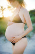 © Dreamwood - Michael & Lucy/Stocksy - Crop pregnant woman in swimwear touching belly