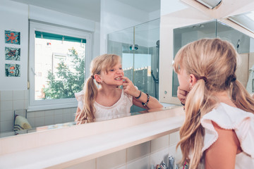 Wall Mural - lovely blond child examining her healthy teeth in mirror in the bathroom