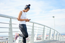 Young Fit Urban Woman Using A Fitness App Whilst Working Out On An Urban Walkway.