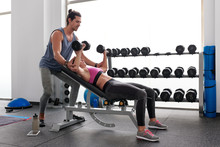 Man Helping Sportswoman With Dumbbell Press On Bench