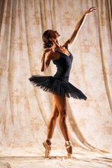 Wall Mural - Full body portrait. Russian ballerina in a black dancing suit is posing in dark studio