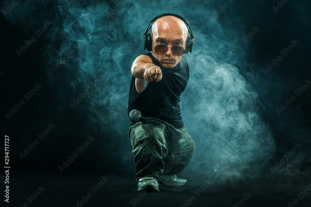Portrait of stylish midget MC in with headphones and sunglasses posing with microphone. - obrazy, fototapety, plakaty 