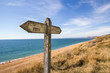 A weather worn wooden sign points the way of the west Dorset coast path along the section near Burton Bradstock and showing Chesil Beach and the shoreline