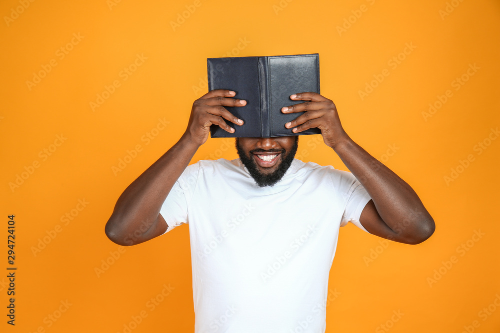 Happy African-American man with book on color background
