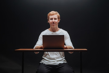 programmer in a white t-shirt on a black background with a laptop