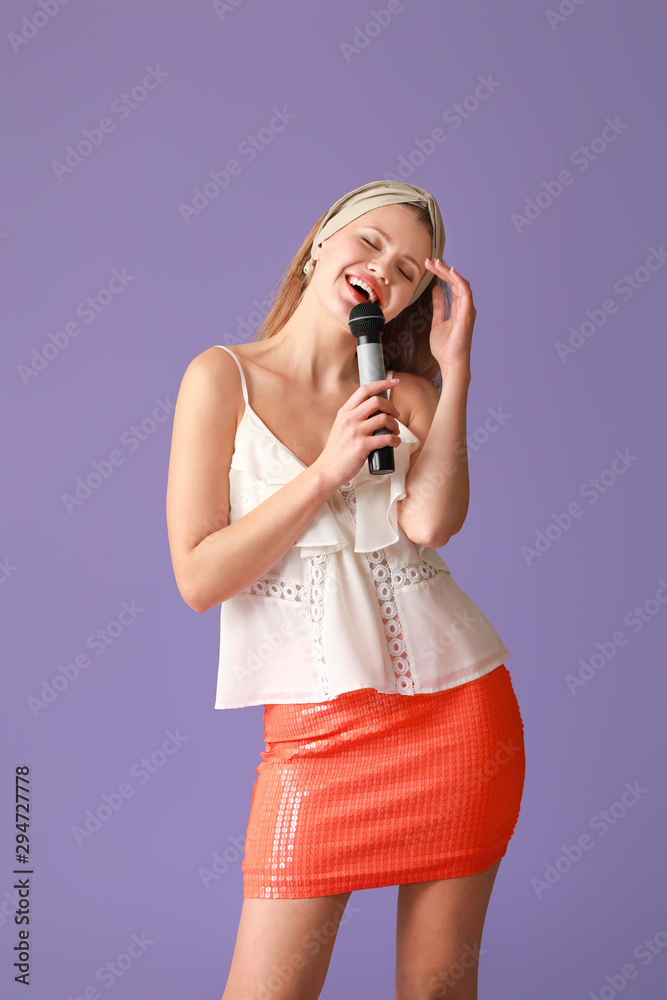 Beautiful young female singer with microphone on color background
