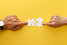 Cropped View Of Woman And Man Matching Pieces Of White Jigsaw Puzzle On Yellow Background