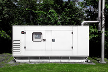 Backup Diesel Electric Power Emergency Generator Mounted On A Green Lawn With Green Trees And A Separate Exhaust Pipe For Environmental Safety.