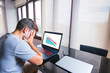 © GENETTICA - Young man at office lamenting with hands on the head in front of computer with financial graph of unsuccessful business on the screen. Arrow going down. Screen graphics are made up.