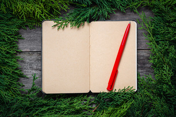 Wall Mural - Christmas frame from fir branches on a background of an old gray board around an open notebook with blank sheets and a red pen. Frame of fir branches. Christmas card blank concept.