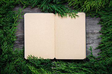 Wall Mural - Christmas frame from fir branches on a background of an old gray board around an open notebook with blank sheets. Frame of fir branches. Christmas card blank concept.